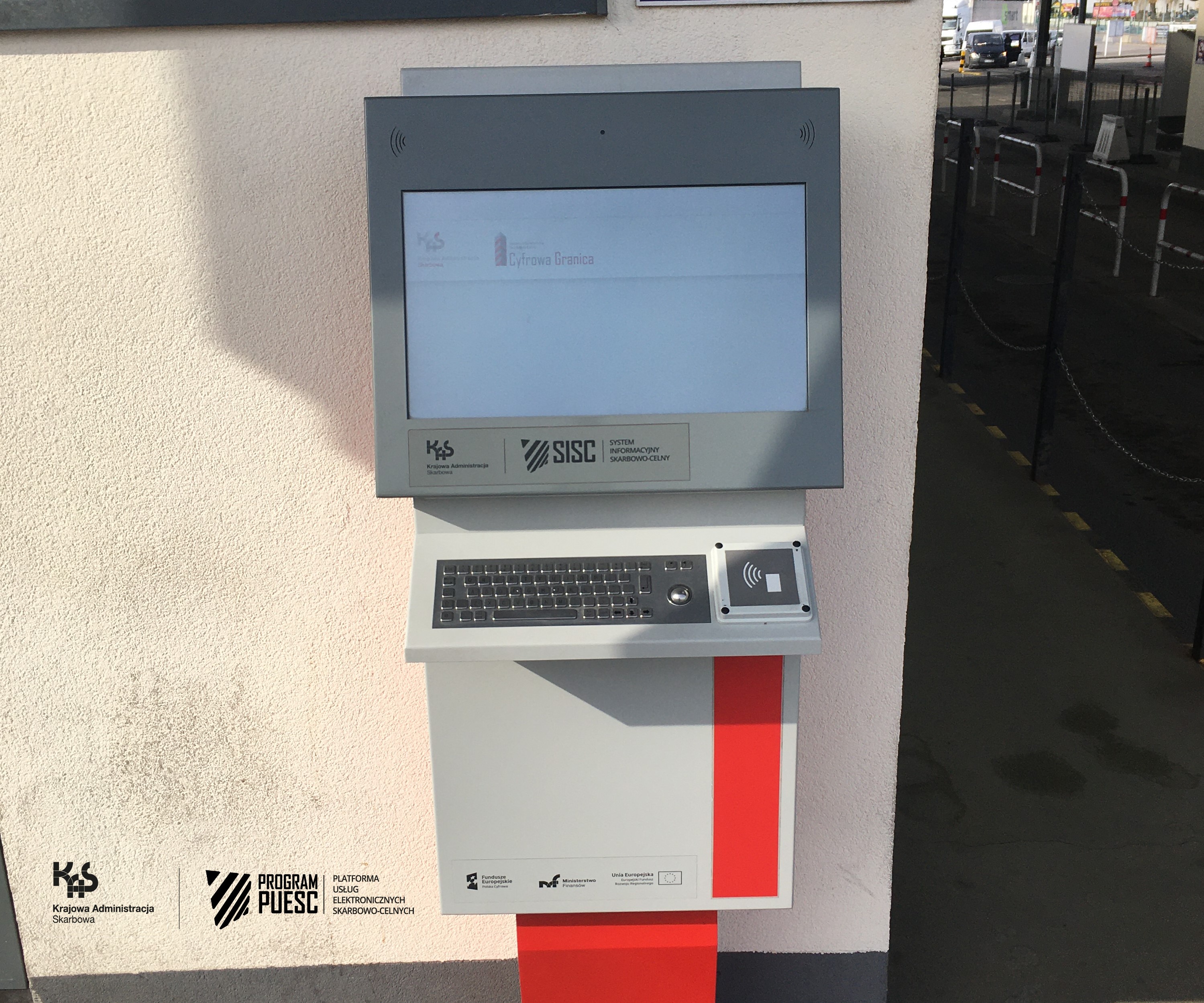 The second type of kiosk - external kiosk within the border crossing point. The device is placed on the wall of the building, consisting of a monitor, keyboard and card reader, on which logos are placed: National Revenue Administration, European Funds Digital Poland, Tax and Customs Information System, Ministry of Finance, European Union European Regional Development Fund.