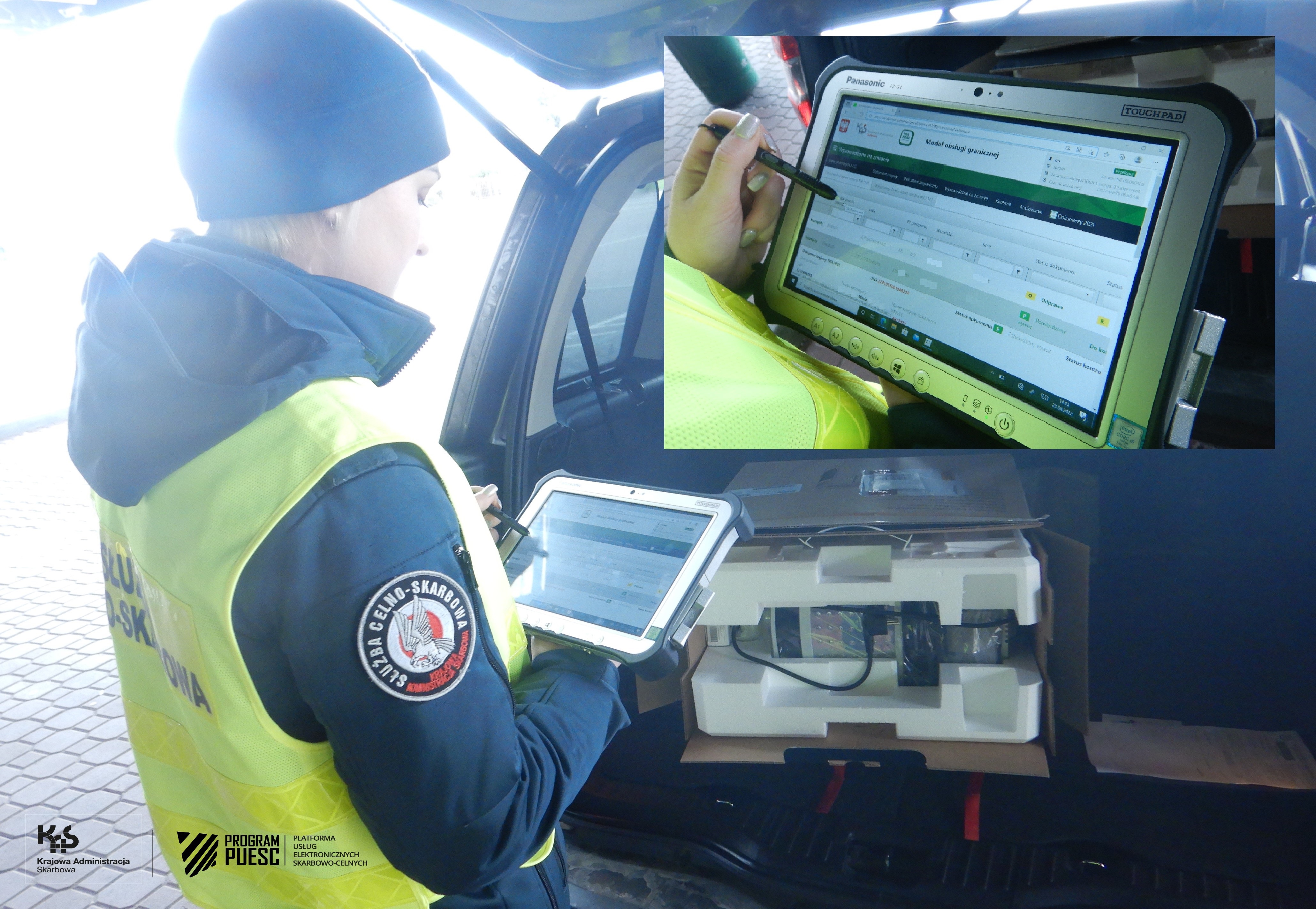 An officer operating a tablet at the border crossing, in the background you can see a car with an open trunk and an open cardboard box inside.